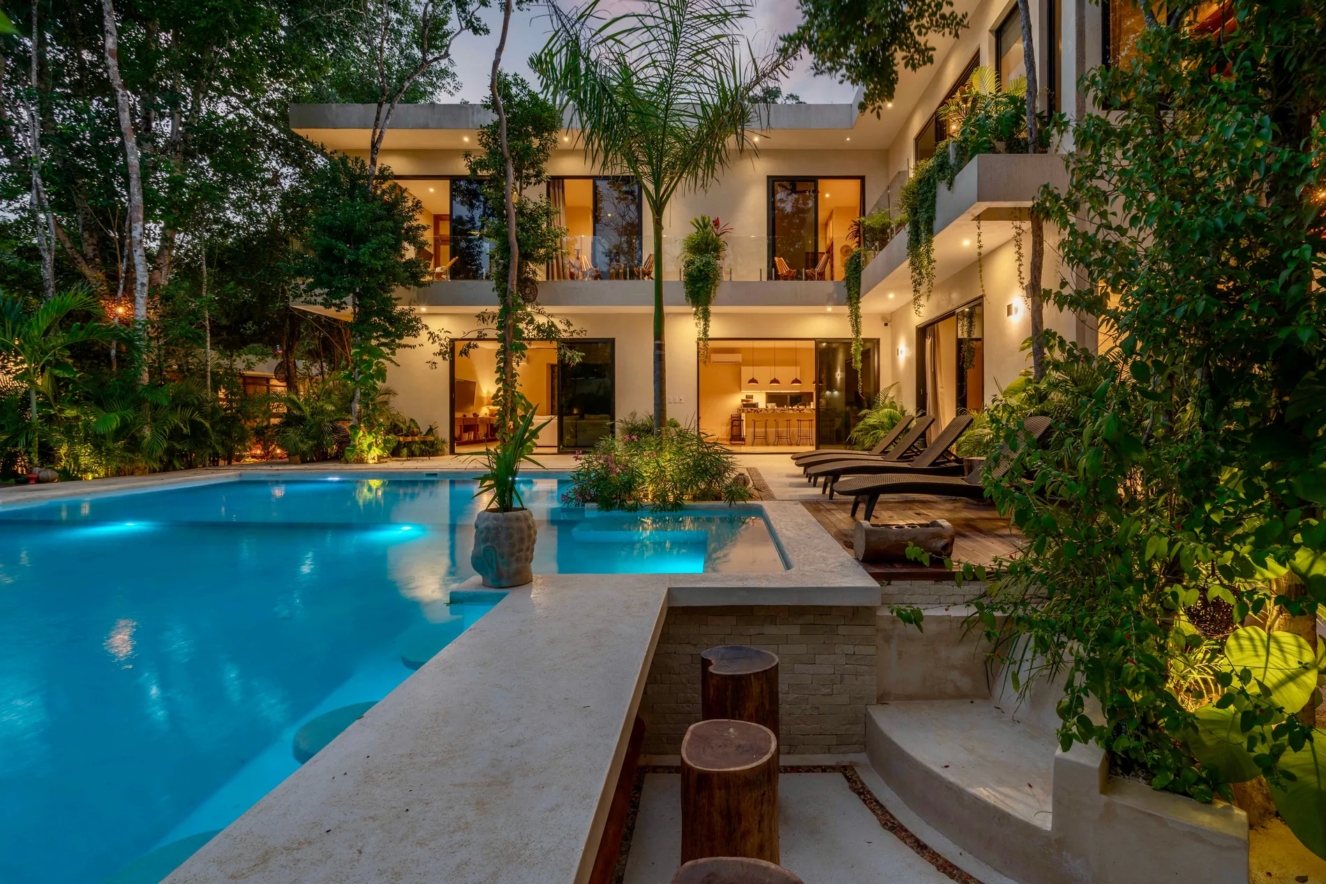 A lit pool and tropical planting behind a modern Los Angeles home at dusk